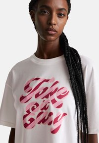 Camiseta blanca de algodón con un gran estampado gráfico rosa que dice "Take it Easy", con un corte relajado y mangas cortas.