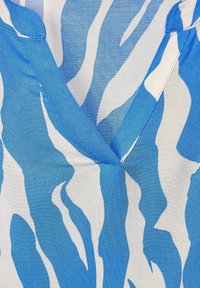 Blå och vit djurmönstrad tyg har en V-ringning med kontrasterande blå sömmar, och visar en slät textur och flödande design.