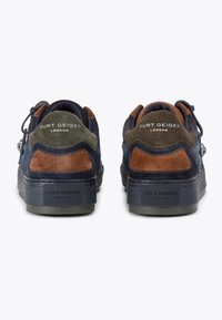 Une paire de baskets en suede navy, vert olive et marron de Kurt Geiger London vues de l'arrière, avec une semelle noire et une marque sur le talon et le dessus.