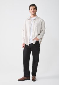 Camisa de botones a rayas beige claro sobre una camiseta blanca, combinada con pantalones negros y botas de tobillo marrones. Diseño minimalista con acentos sutiles.