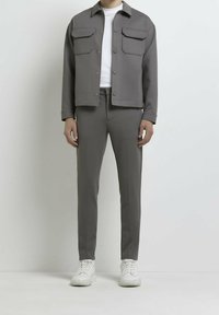 Szary jacket z dwiema dużymi kieszeniami, zestawiony z dopasowanymi szarymi spodniami i białymi sneakersami. Gładka tekstura materiału, casualowy design.