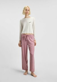 Witte lange mouwen top met een gegolfde zoom, gecombineerd met lichtroze gestreepte broek met een trekkoord in de taille en gegolfde manchetten.