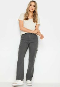 Licht beige V-hals t-shirt gecombineerd met hoogoplopende grijze cargobroek met voorzakken en taps toelopende pijpen, aangevuld met witte sneakers.