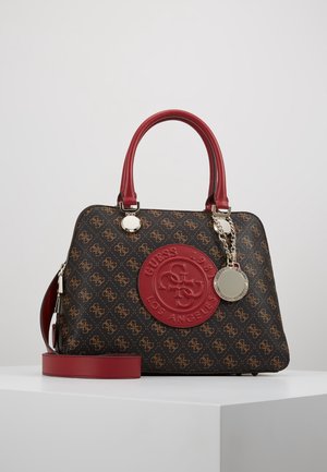 Brown and red Guess handbag with patterned logo, red handles, detachable strap, and silver circular charm on a white surface.