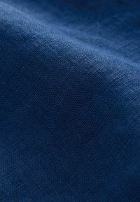 Gros plan sur un tissu bleu texturé avec un motif de tissage visible et des reflets lumineux subtils.