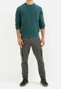 Morski sweter dziany o ribbnowym splocie, zestawiony z szarymi spodniami cargo posiadającymi boczne kieszenie, dopełniony ciemnoszarymi zamszowymi sneakersami.