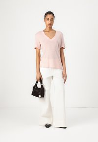 Top rosa chiaro a maniche corte con scollatura a V dal taglio morbido, abbinato a pantaloni bianchi a gamba larga e una piccola borsa nera. Tessuto semplice, stile casual.