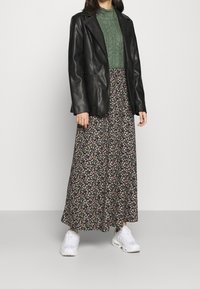 Blazer en cuir noir, pull en tricot vert, jupe maxi florale noire avec des détails roses et verts, et baskets blanches. Textures douces.