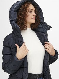 Doudoune bleu marine, dotée d'une capuche, d'un design matelassé et d'une fermeture éclair argentée. Portée sur un haut à côtes blanc et un jean bleu.