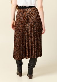 Gonna plissettata marrone con stampa a leopardo nera, vita elastica, che arriva sotto il ginocchio, abbinata a stivali neri alti fino al ginocchio.