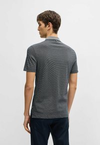 Polo a maniche corte di colore grigio scuro con un motivo testurizzato, caratterizzato da un colletto a contrasto e un sottile accento in metallo sul collo.