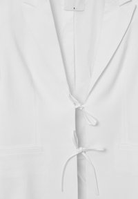 Blazer bianco con revers a punte, chiusura con cravatta e due tasche frontali. Tessuto liscio e design minimalista. Etichetta della taglia visibile all'interno.
