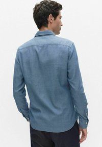 Lichtblauw denim shirt met lange mouwen, knoopmanchetten en een omvouwbare kraag. Gladde textuur, licht getailleerd ontwerp.