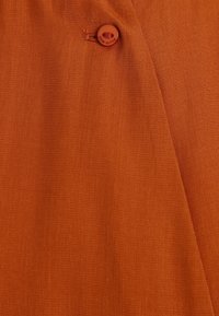 Tela de color óxido con una textura suave, que presenta un solo botón cosido con el texto "mío para mí" cerca del borde.