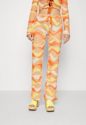 Conjunto de dois peças com um top curto e calças largas num padrão de ondas multicolorido em laranja, amarelo e bege. O material parece texturizado.