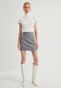 Vit randig polotröja, grå åtsittande minikjol och knälånga vita stövlar med texturfinish och blockklack, med fokus på rena linjer.