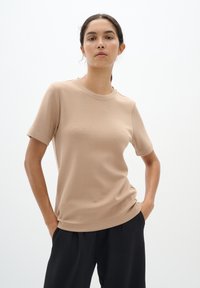 Beige, rövid ujjú póló, kerek nyakkivágással, puha anyagból készült. Sima textura, laza fazon, fekete nadrággal párosítva.