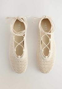 Lace-up ballet flats vaaleasta kudotusta materiaalista, joissa on suljettu varsi, monimutkainen kudottu pinta ja litteä pohja pyöreillä reunoilla.
