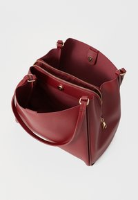 Borsa a tracolla in pelle rossa con dettagli in oro. Presenta un compartimento con zip e una parte superiore aperta. Texture liscia e forma strutturata.