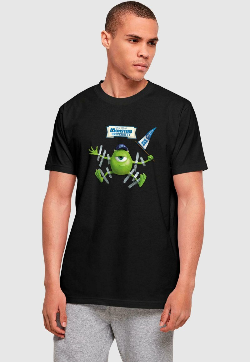Melna kokvilnas T-krekls ar grafiku, kurā attēlots zaļš varonis no Monsters University, ko ieskauj zili un balti reklāmas uzraksti.