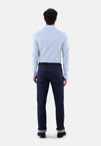 Helles blaues Langarmhemd kombiniert mit dunkelblauen Jeans, mit einer glatten Textur und aufgerollten Manschetten. Klassisches Design mit standardmäßigen Gesäßtaschen.