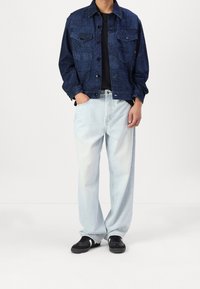 Jeansjacka med en texturerad mörkblå yta, i kombination med ljusblå, löst sittande jeans och svarta sneakers. Minimalistisk design och klassisk passform.