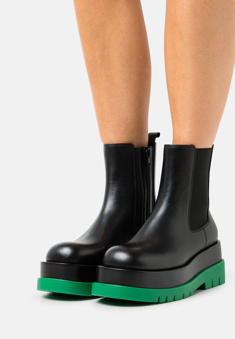 Bottines en cuir noir avec semelles plateformes épaisses et semelles extérieures robustes vert vif portées sur des jambes nues.