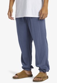 Blå bomullsjoggingbyxor med elastiska mudd och en avslappnad passform, ihopparade med bruna mockasandaler med platt sula och minimalistisk design.