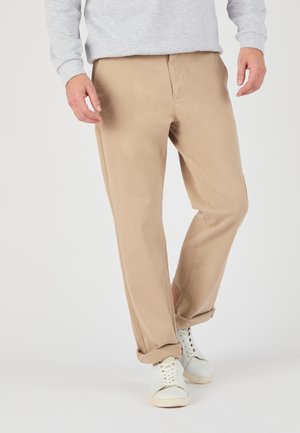 Khaki Chino-Hosen mit geradem Bein, aus leichtem Stoff, mit seitlichen Taschen und umgeschlagenen Säumen, kombiniert mit weißen Sneakers.