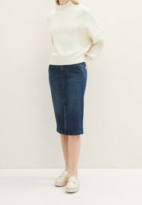 Suéter de punto acanalado color crema con cuello alto, combinado con una falda lápiz de mezclilla oscura y zapatos tipo slip-on de color claro. Textura suave, silueta ajustada.