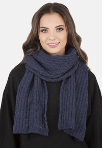 Kötött, sötétkék sál, texturált bordás mintával, puha anyagból, a nyak köré drapírozva. A végégek laza módon lógnak le.