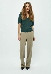 Suéter de manga corta verde oscuro con escote en V, combinado con pantalones de pierna ancha beige claro y zapatos negros de punta. Textura suave en toda la prenda.