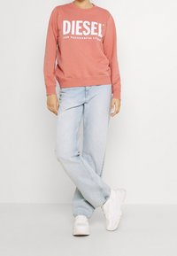 Rosa Sweatshirt mit weißem Text "DIESEL FOR SUCCESSFUL LIVING", kombiniert mit hellblauen Jeans und weißen Sneakers. Lässiger Schnitt und weiche Textur.
