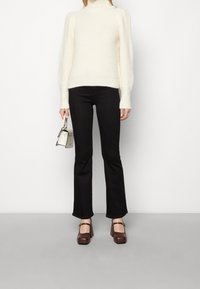 Maglione a collo alto color crema con lavorazione a maglia testurizzata e maniche a sbuffo; abbinato a jeans a zampa neri e scarpe con tacco a blocco marroni. Piccola borsa a mano.