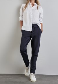 White button-up shirt with rolled sleeves, paired with navy jogger pants featuring drawstring waist. Footwear: white athletic shoes.