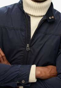 Granatowa bomberka z zamkiem błyskawicznym z przodu, stojącym kołnierzem i kremowym prążkowanym golfem. Posiada zatrzaski i prążkowane mankiety.