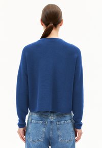 Blauer, strukturierter Strickpullover mit einem verkürzten Design, langen Ärmeln und einem runden Ausschnitt, kombiniert mit hochgeschnittenen, hellblauen Jeans.