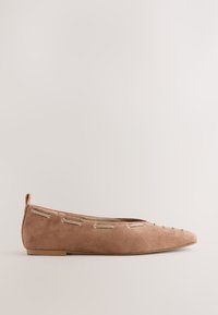 Chaussure plate en daim marron à bout pointu avec des œillets métalliques le long des côtés et une petite languette au talon.