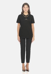 T-shirt nera in cotone con maniche corte, con stampa del logo in oro. Abbinata a pantaloni neri aderenti e décolleté lucide con punta appuntita.