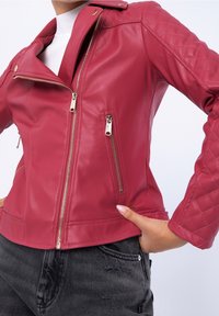Červená motocyklová bunda z umělé kůže s přiléhavým střihem, asymetrickým zipem, prošívanými ramenními akcenty a dvěma zipovými kapsami.