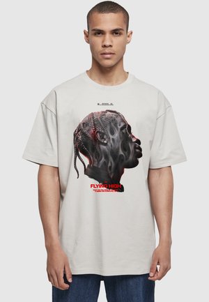 Young man with short hair wears light gray T-shirt featuring side profile of a person with braided hair and red text "Flying High."