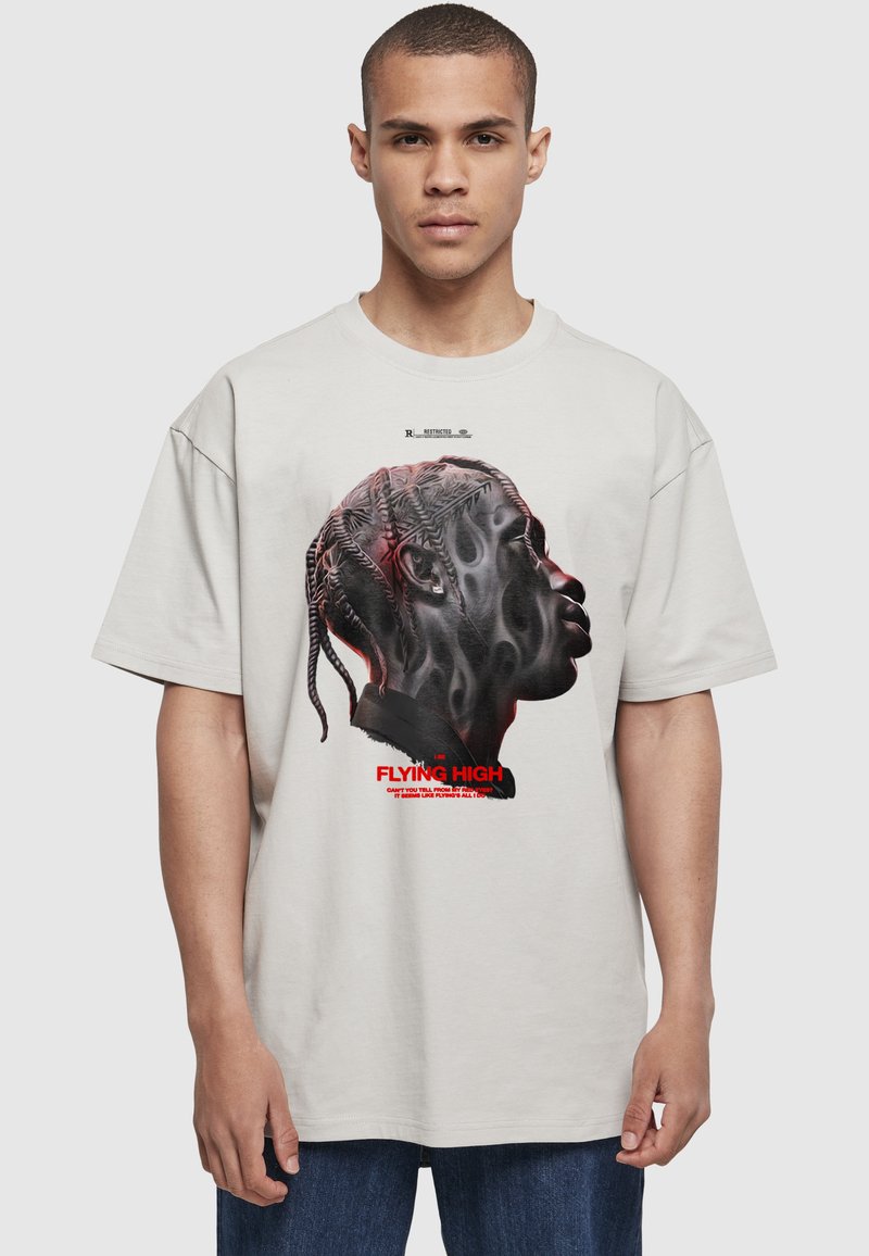 Ung mand med kort hår iført lysegrå T-shirt med sideprofil af en person med flettet hår og rød tekst "Flying High."