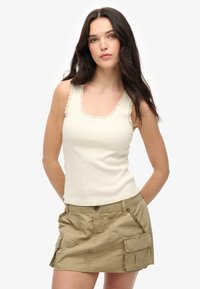 Crème tanktop met geschulpte kantafwerking bij de halslijn en schouders, gecombineerd met een khaki cargominirok met zijzakken en knoopsluiting.