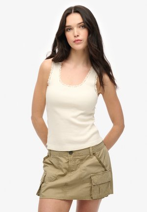Crème tanktop met geschulpte kantafwerking bij de halslijn en schouders, gecombineerd met een khaki cargominirok met zijzakken en knoopsluiting.