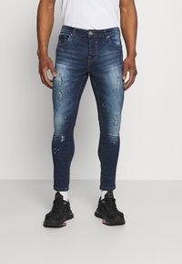 Skinny-fit dark blue jeans, featuring distressed details, a classic five-pocket design, and contrast stitching. Fabric appears denim with slight sheen.