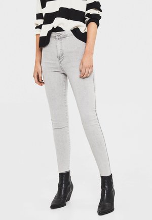 Jean skinny gris taille haute, avec une texture délavée et des coutures noires contrastées. Associés à des bottines noires.