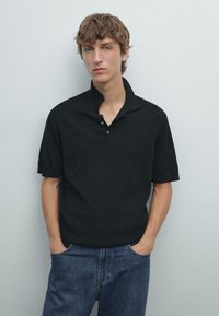 Svart ribbad polo skjorta med delvis öppen krage och korta ärmar, matchad med blå denim jeans. Enkelt mönster, inga dekorationer eller mönster.