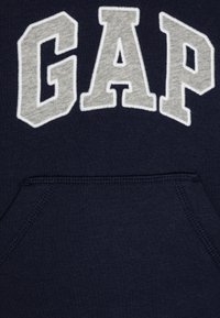 Ναυτικό μπλε φούτερ με μεγάλο, ραμμένο γκρι γράμμα "GAP" στο στήθος. Περιλαμβάνει μπροστινή τσέπη και απαλή, υφασματική υφή.