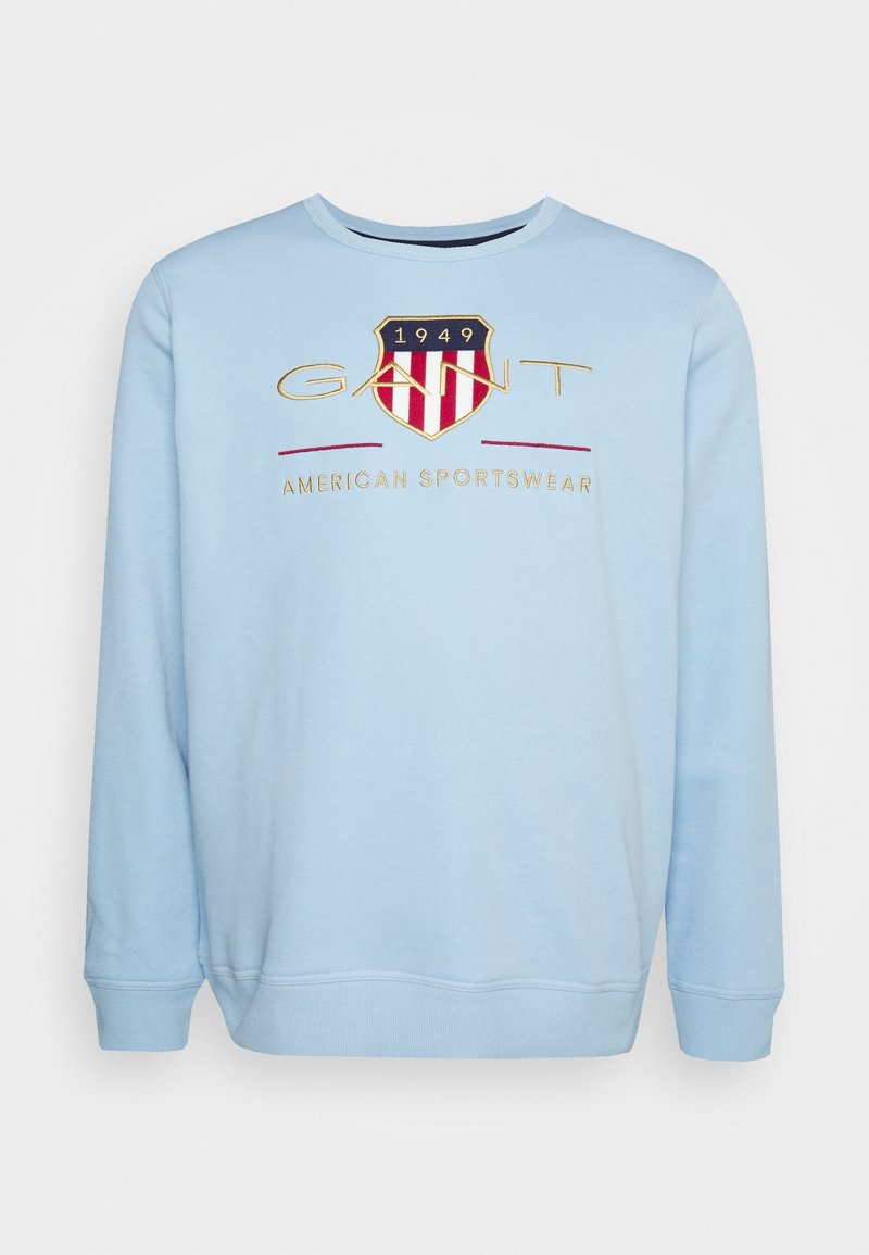 Sweat-shirt bleu clair à col rond, avec un logo en forme de bouclier rouge et blanc et le texte «GANT 1949 American Sportswear» sur la poitrine.