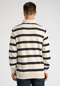 Polo z długim rękawem w kremowe i granatowe paski, z kołnierzykiem, ściągaczami na mankietach i luźnym krojem. Gładka tkanina o jednolitej fakturze.